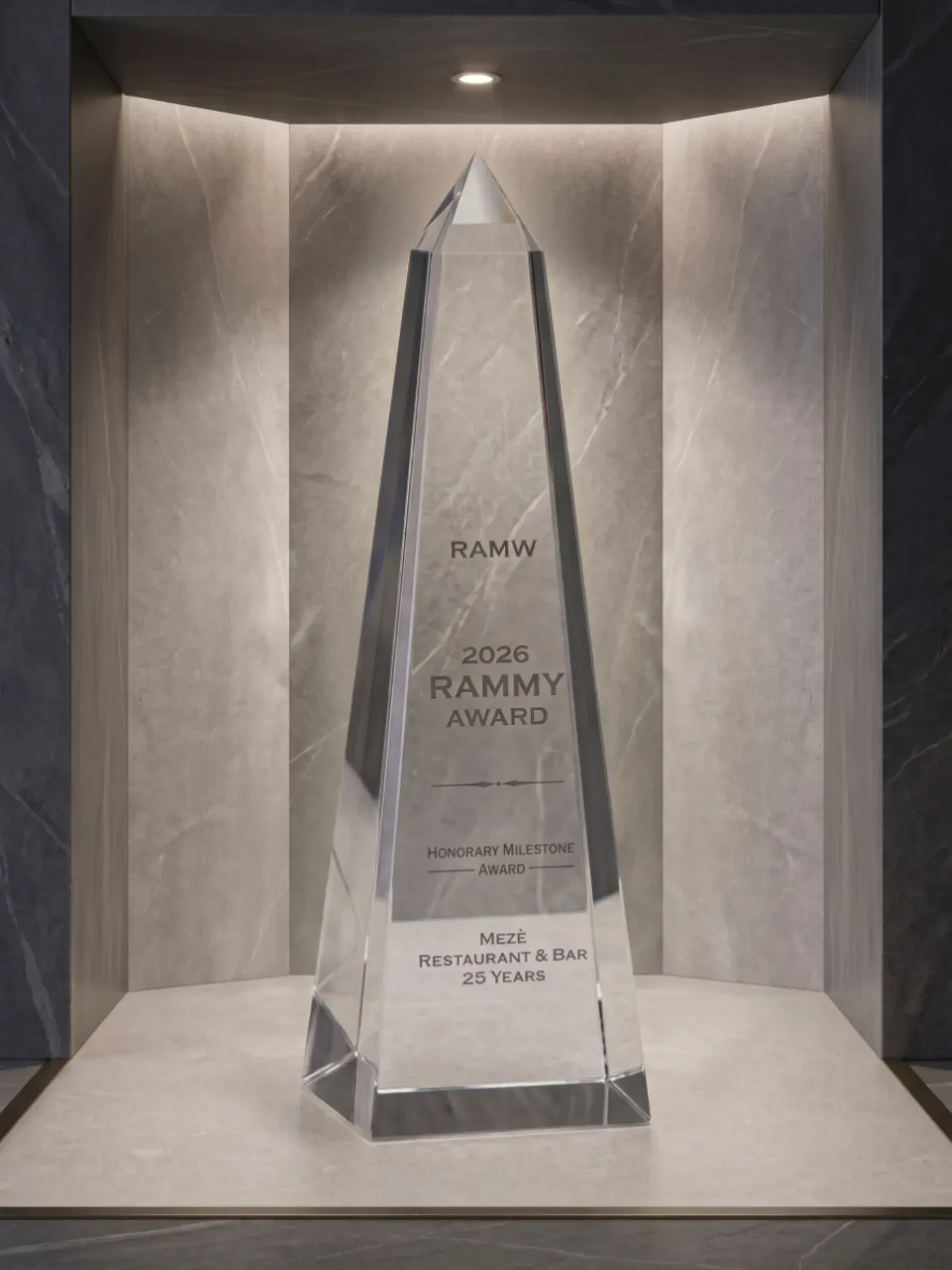 The 2026 RAMMY Honorary Milestone Award, a crystal obelisk engraved for Mezè Restaurant & Bar's 25 years, lit in a stone display niche